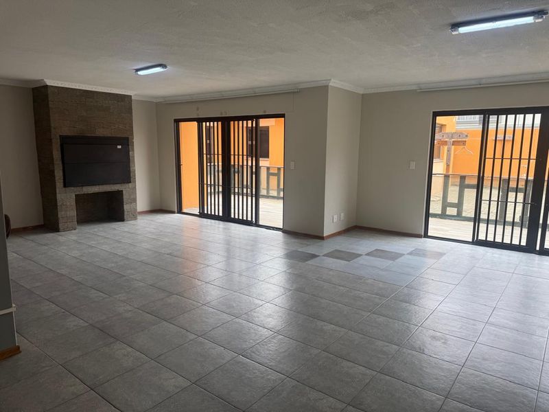 Spacious, empty living area featuring a built-in stone-clad fireplace, tiled flooring, and large sliding doors providing access to the exterior.
