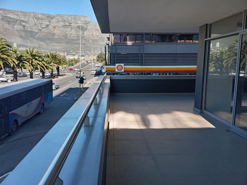 A spacious covered balcony featuring tiled flooring and metal railings, offering an elevated view of the street and surrounding mountain landscape.
