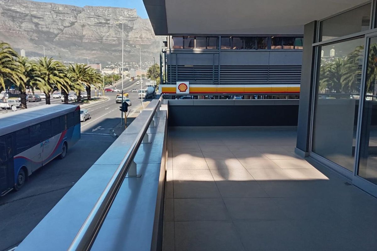 A spacious covered balcony featuring tiled flooring and metal railings, offering an elevated view of the street and surrounding mountain landscape.