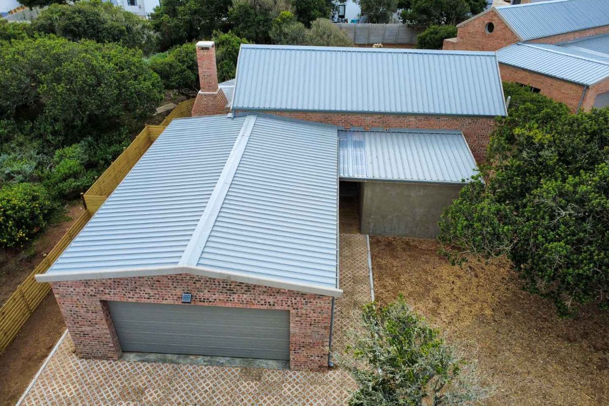 Aerial view of a townhouse featuring a brick facade, metal roof, and a paved driveway leading to a single garage.