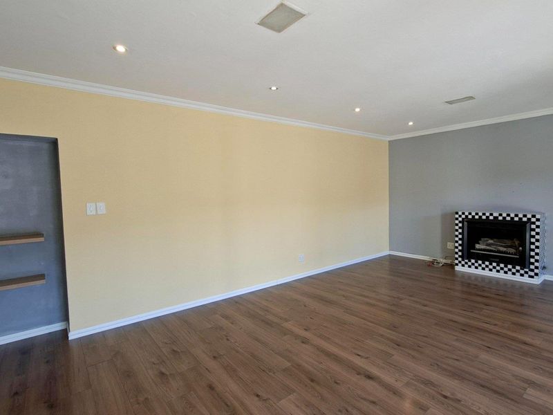 Spacious living room featuring laminate flooring, recessed downlights, and a distinctive checkered-tile built-in fireplace, offering a clean and versatile living space.