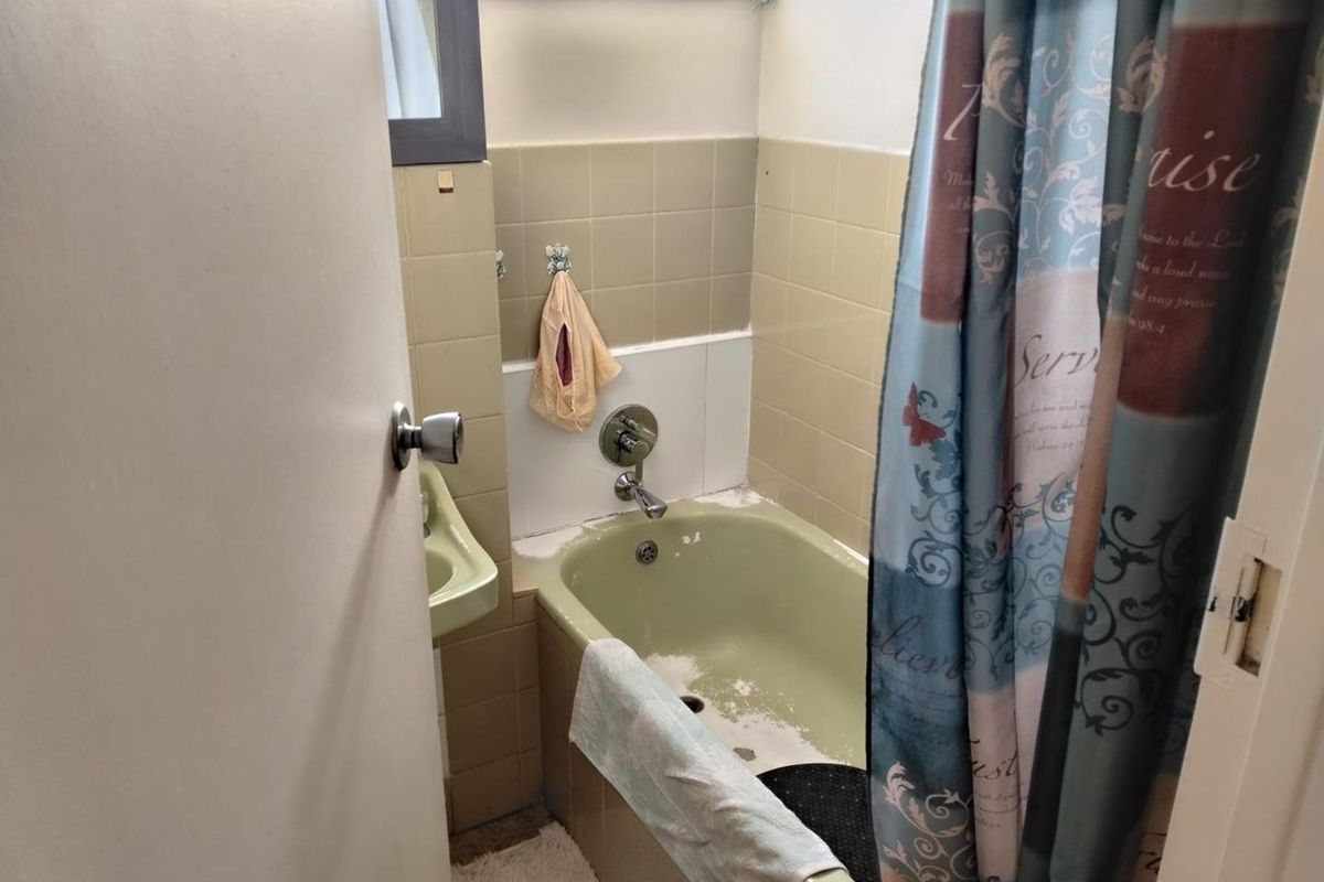A compact bathroom featuring a dated green bathtub, matching basin, and neutral wall tiles, requiring cosmetic updates to modernize the space.