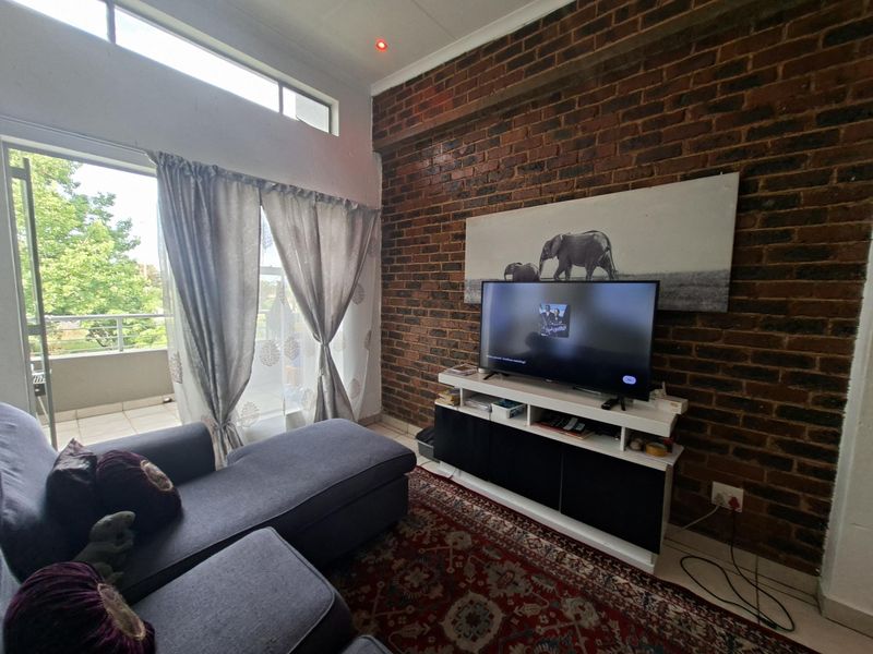 A cozy living room featuring an exposed brick wall, high clerestory windows for natural light, and direct access to a private balcony.