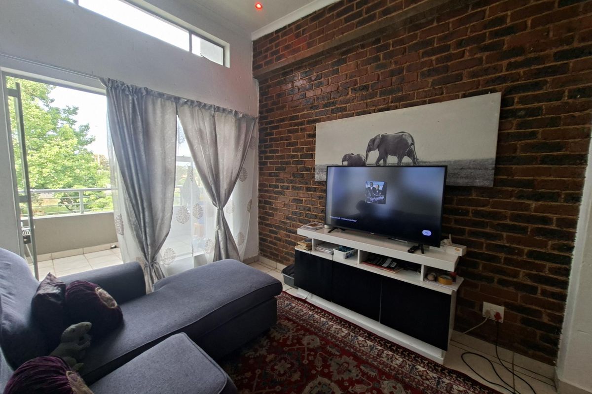 A cozy living room featuring an exposed brick wall, high clerestory windows for natural light, and direct access to a private balcony.