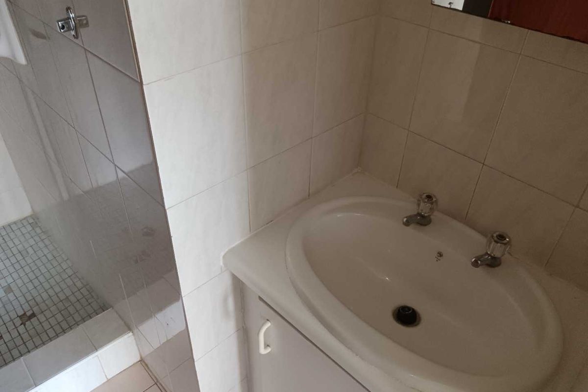A functional bathroom featuring a vanity cabinet with a ceramic basin and a separate shower enclosure with tiled walls and flooring.