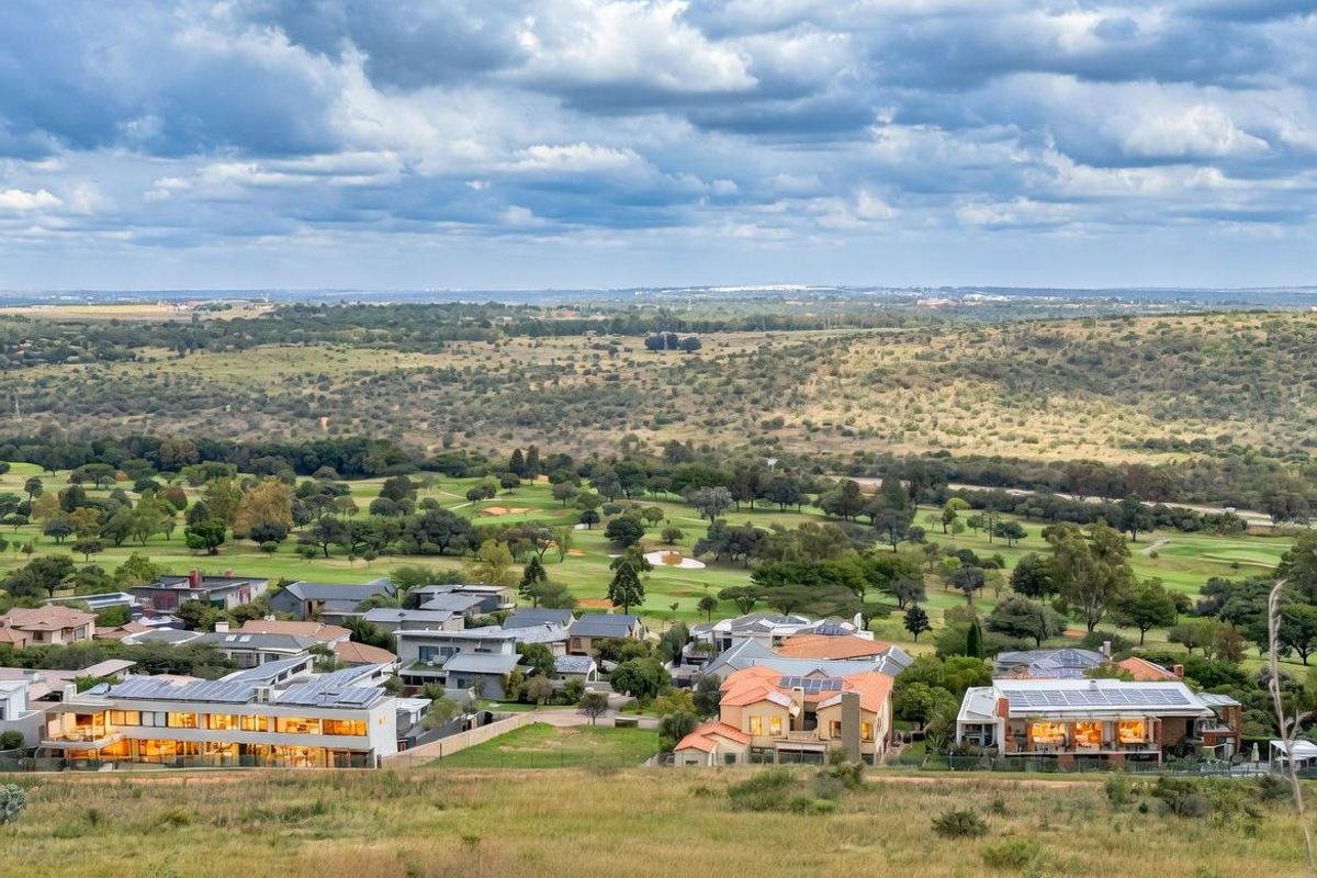 An elevated aerial view showcasing a residential estate nestled within a scenic landscape, featuring modern homes with solar panels and expansive green surroundings.