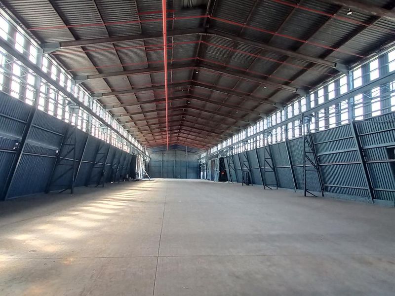 Spacious industrial warehouse featuring a high-clearance steel portal frame, concrete flooring, fire sprinkler system, and extensive natural light from clerestory windows.