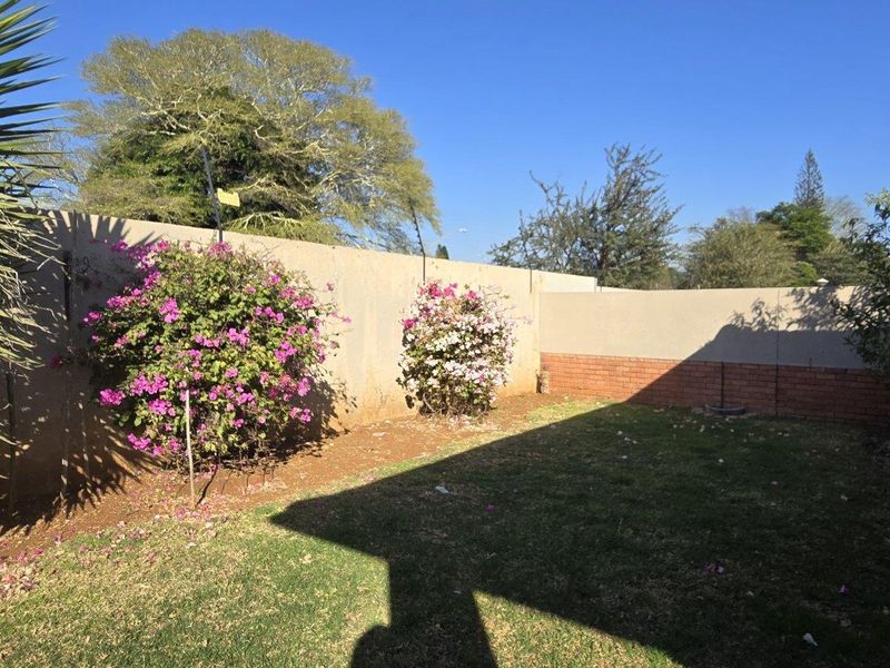 A private rear garden area featuring a lawn, perimeter boundary wall with brick detailing, and a paved walkway alongside the townhouse structure.