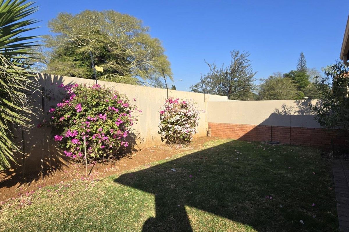 A private rear garden area featuring a lawn, perimeter boundary wall with brick detailing, and a paved walkway alongside the townhouse structure.