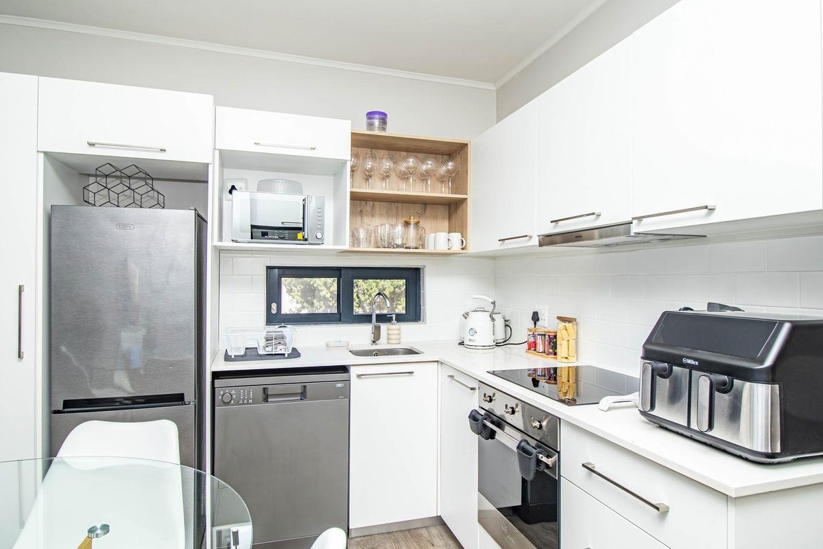 Modern kitchen featuring white cabinetry, stone countertops, subway tile backsplash, integrated oven, hob, extractor fan, and space for a dishwasher.