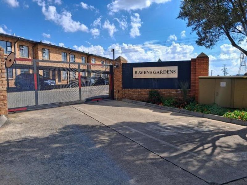 The entrance to Ravens Gardens apartment complex featuring a secure sliding gate, brick boundary wall, and paved driveway access.