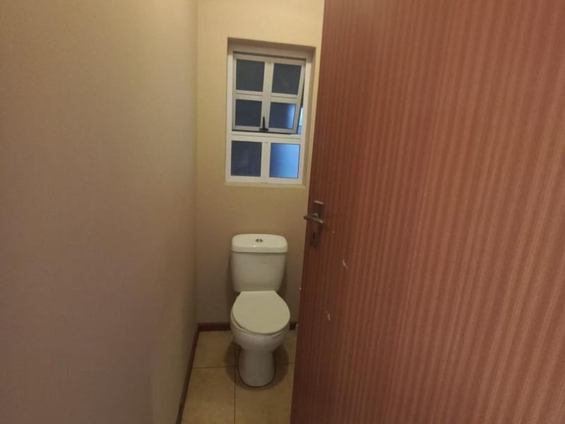 A compact, functional bathroom featuring tiled flooring, a standard toilet, and a small window for natural light.