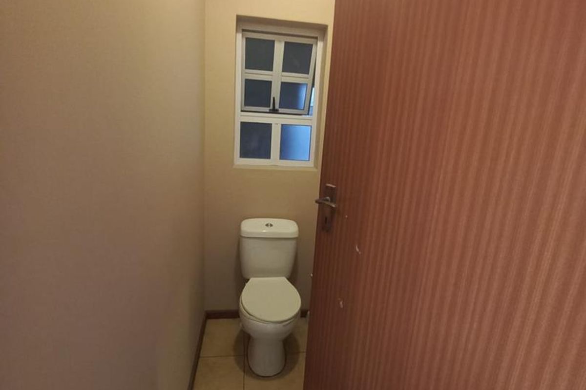 A compact, functional bathroom featuring tiled flooring, a standard toilet, and a small window for natural light.