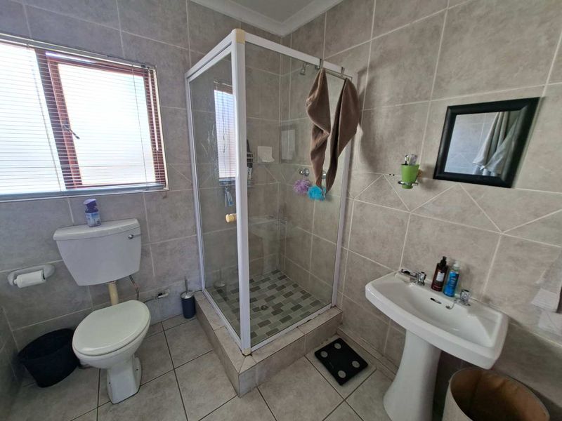 A functional bathroom featuring a shower enclosure, pedestal basin, and toilet with neutral wall and floor tiling.