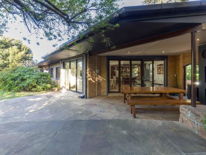 Spacious covered patio featuring stone paving, a built-in braai, and large sliding glass doors providing seamless access to the interior living areas.