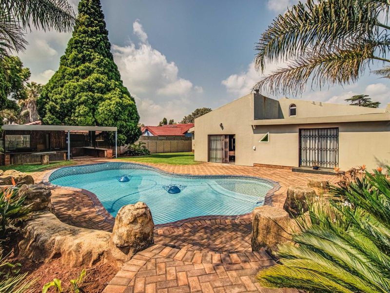 A well-maintained outdoor area featuring a swimming pool with brick paving, a covered patio, and established garden landscaping.