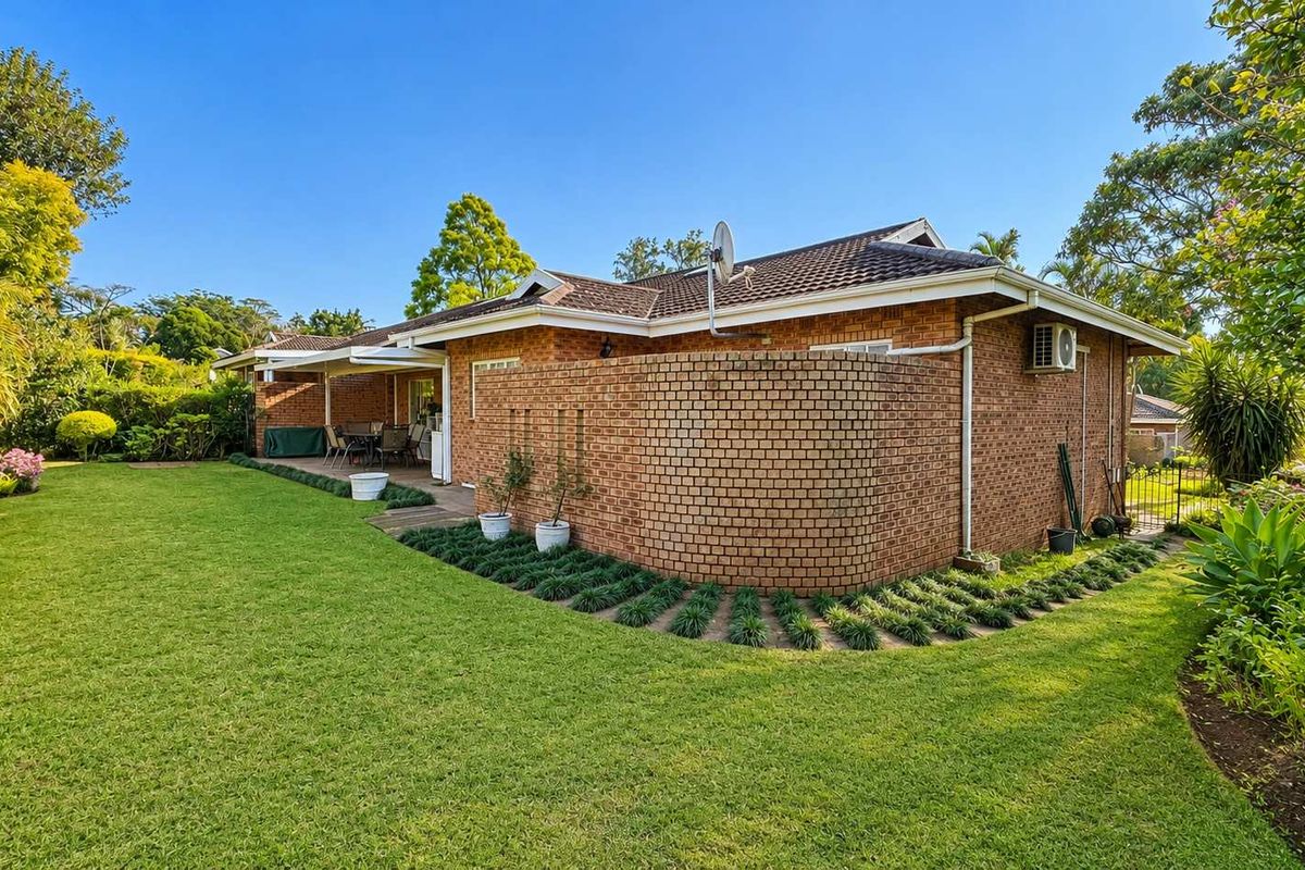 A well-maintained rear exterior view of the townhouse featuring a brick facade, a covered patio area, and a spacious, landscaped garden.