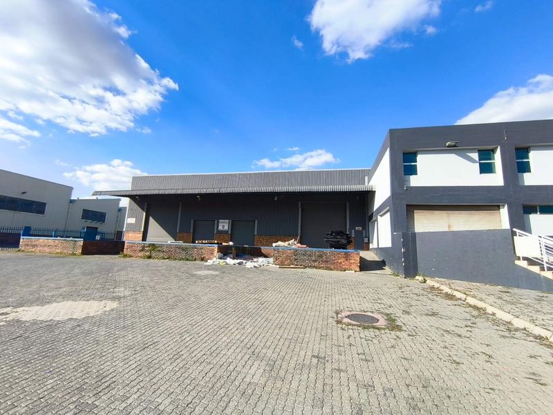 Industrial warehouse exterior featuring a paved loading yard, multiple roller shutter doors, and a raised loading dock area.
