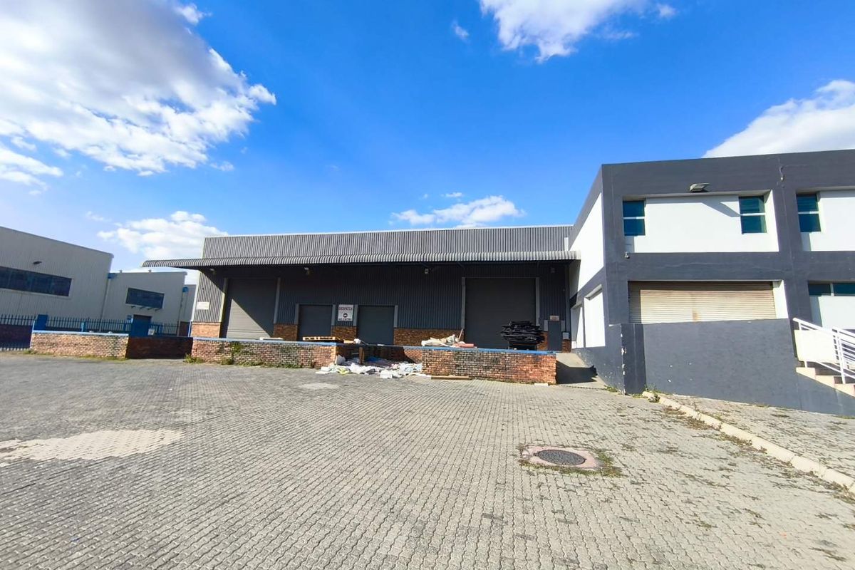 Industrial warehouse exterior featuring a paved loading yard, multiple roller shutter doors, and a raised loading dock area.