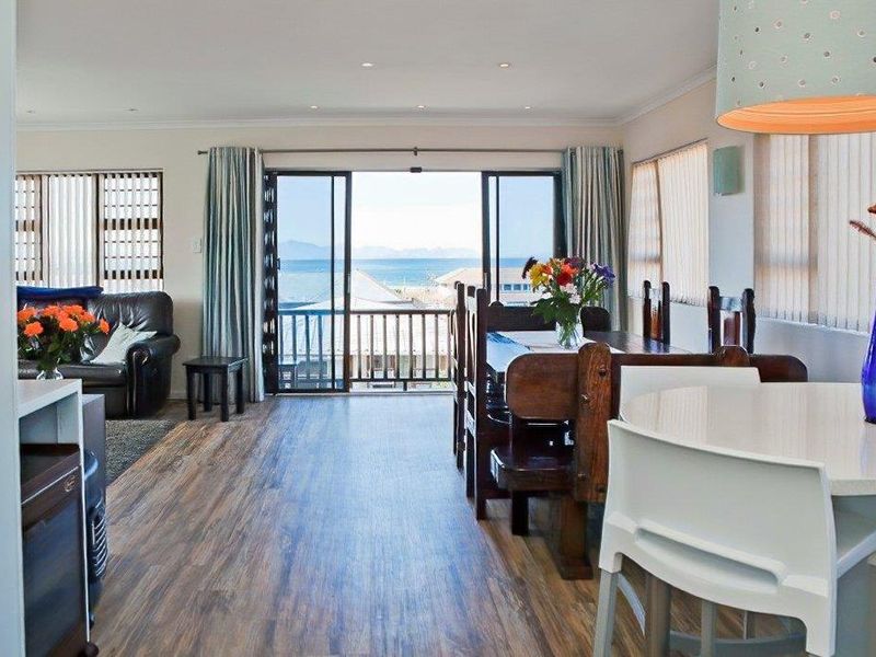 Open-plan living and dining area featuring laminate flooring, recessed lighting, and large sliding doors opening onto a balcony with ocean views.