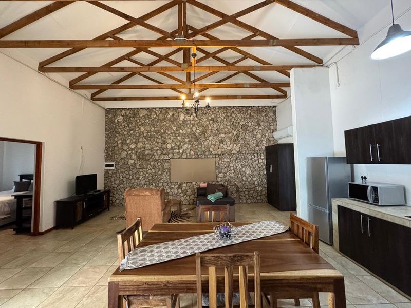 Spacious open-plan living and dining area featuring a striking stone feature wall, exposed timber roof trusses, and integrated kitchen cabinetry.