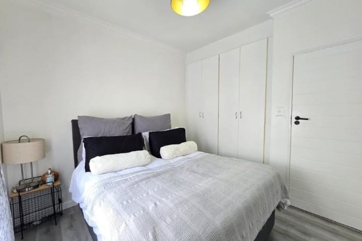 A bright bedroom featuring built-in cupboards, modern grey wood-look flooring, and a contemporary pendant light fixture.