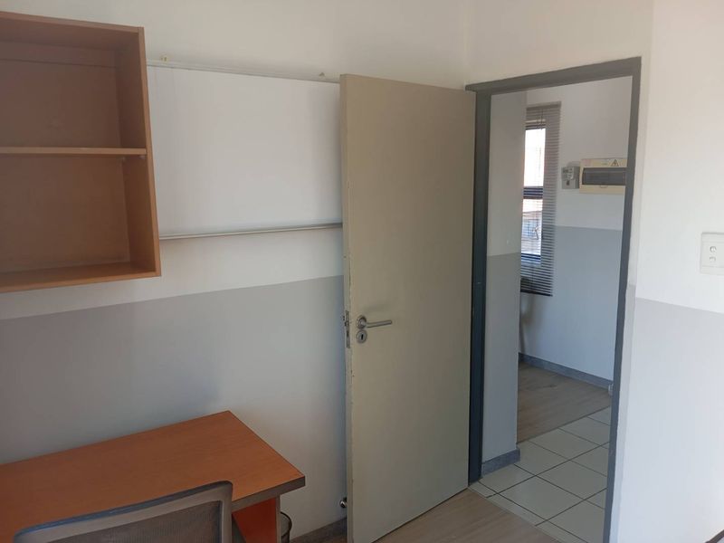 A functional office space featuring built-in shelving and neutral wall finishes, with an adjacent tiled hallway area visible through the doorway.