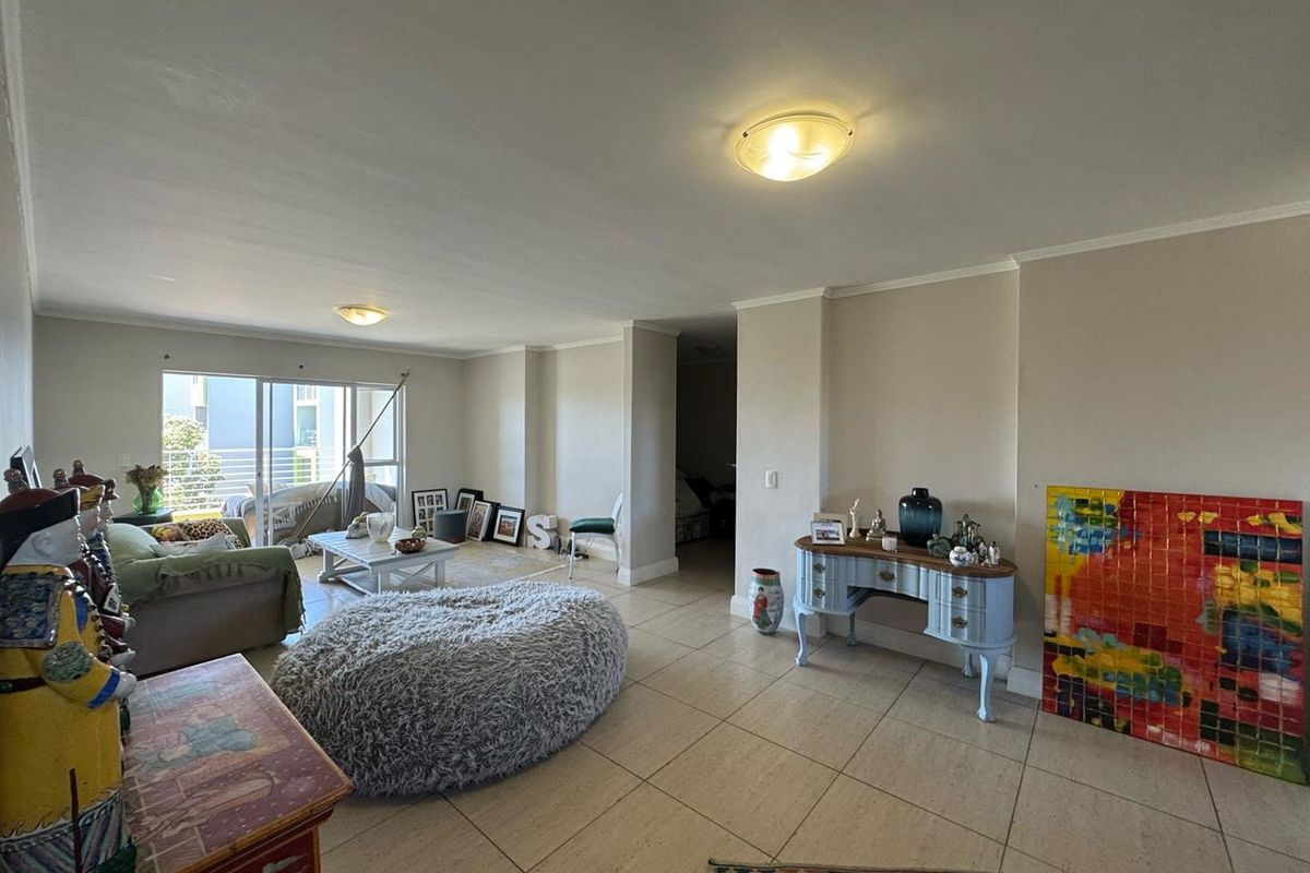 Spacious open-plan living area featuring neutral tiled flooring, coving, and large sliding glass doors providing access to the balcony.