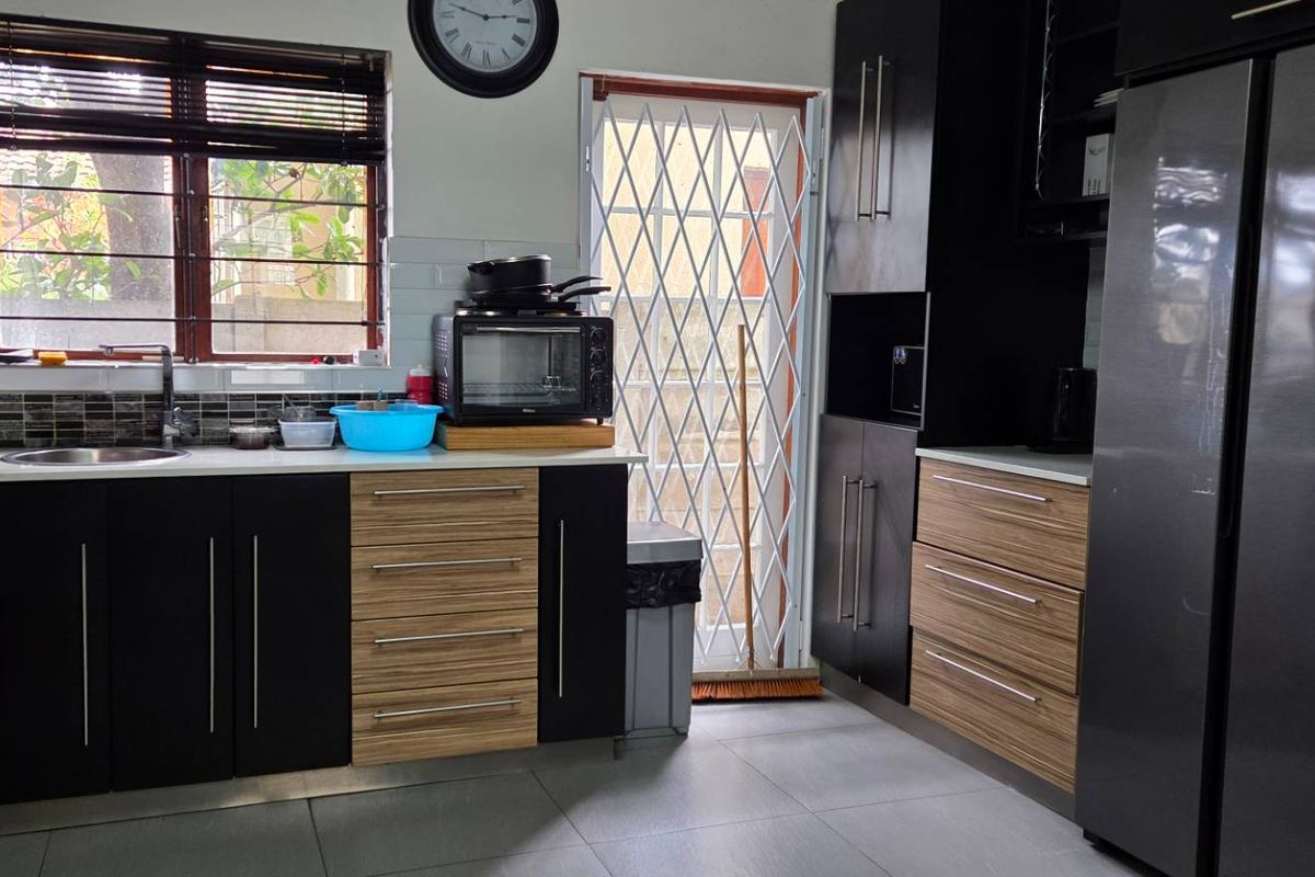 Modern kitchen featuring dark and wood-tone cabinetry, gas stove, stainless steel sink, tiled backsplash, and direct access to the exterior via a security gate.