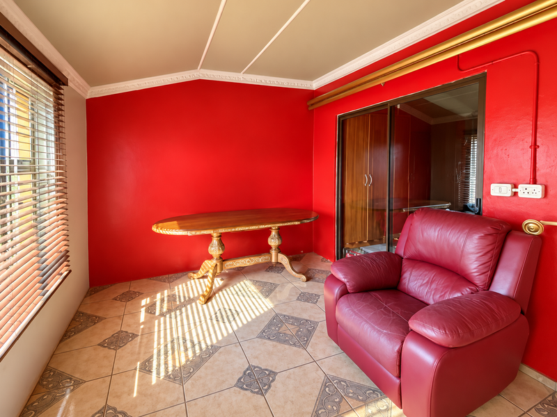 A living area featuring bold red walls, tiled flooring, and a sliding glass door, providing a distinct space with natural light through venetian blinds.