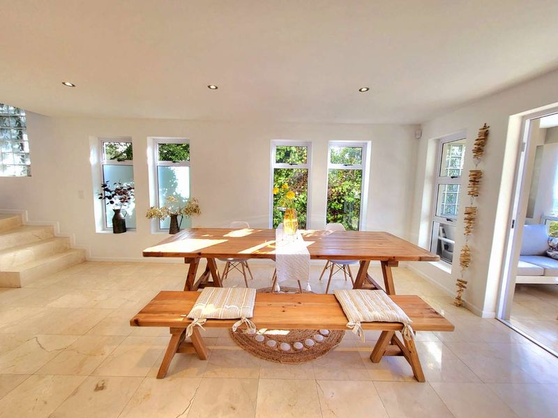 Bright and spacious dining area featuring neutral stone flooring, recessed lighting, and large windows that provide ample natural light and garden views.