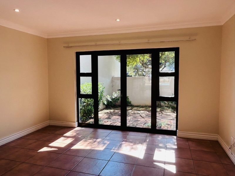 An empty living room featuring tiled flooring, recessed downlights, and large black aluminium framed glass doors opening onto a private paved courtyard.