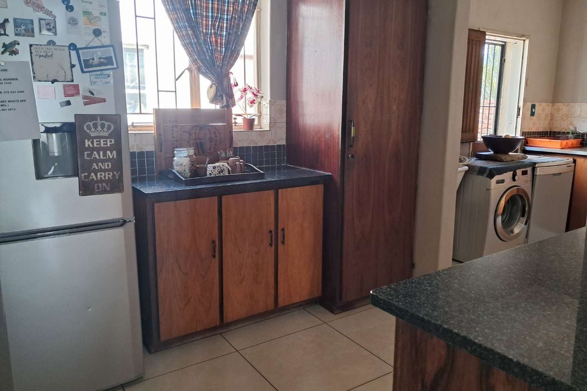 A functional kitchen area featuring wood-finish cabinetry, dark countertops, tiled flooring, and integrated space for laundry appliances.