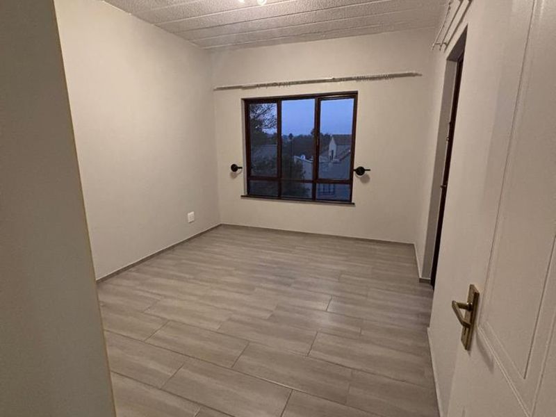 A bright, empty bedroom featuring modern light-toned tiled flooring, a textured ceiling, and a window providing natural light.
