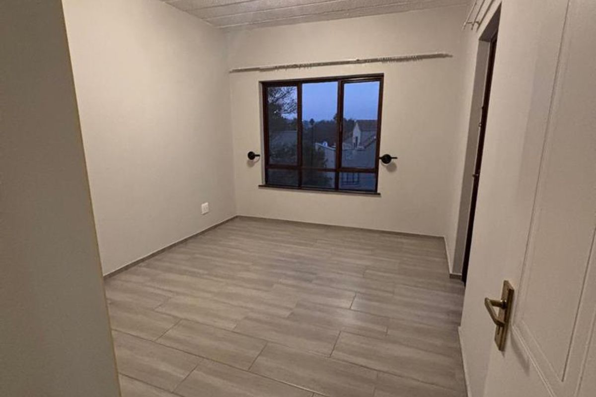 A bright, empty bedroom featuring modern light-toned tiled flooring, a textured ceiling, and a window providing natural light.