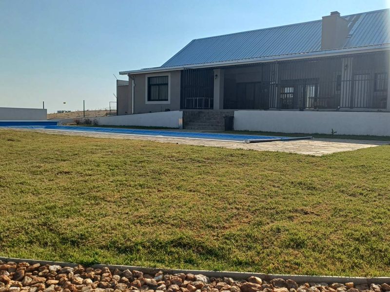 Rear view of the property featuring a spacious lawn, a swimming pool with a cover, and a stone patio area.