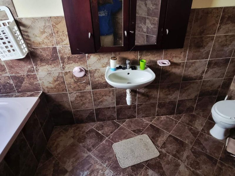 A dated bathroom featuring a built-in bathtub, wall-mounted basin, and toilet, finished with brown ceramic wall and floor tiles.
