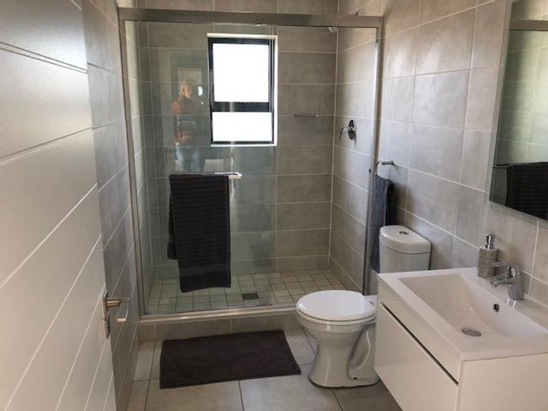 Modern bathroom featuring a glass-enclosed shower, wall-mounted vanity with basin, and neutral tiled finishes throughout.