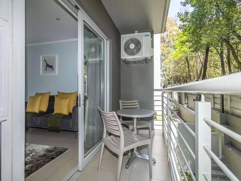 A covered balcony featuring tiled flooring, a metal balustrade, and a wall-mounted air conditioning unit, providing a seamless transition from the living area.