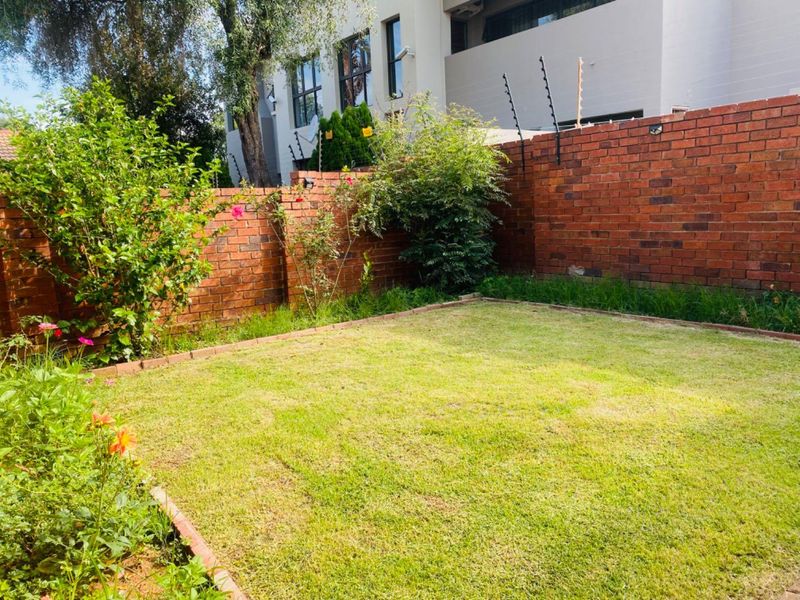 A private rear garden featuring a well-maintained lawn, established flower beds, and a secure brick boundary wall with electric fencing.