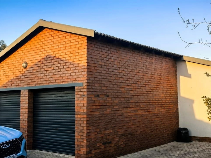 A well-maintained double garage featuring face brick exterior walls, dark roller doors, and a paved driveway area.