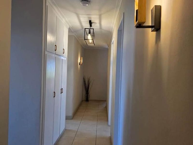 A well-lit hallway featuring neutral floor tiles, built-in storage cabinetry, and modern wall-mounted lighting fixtures.