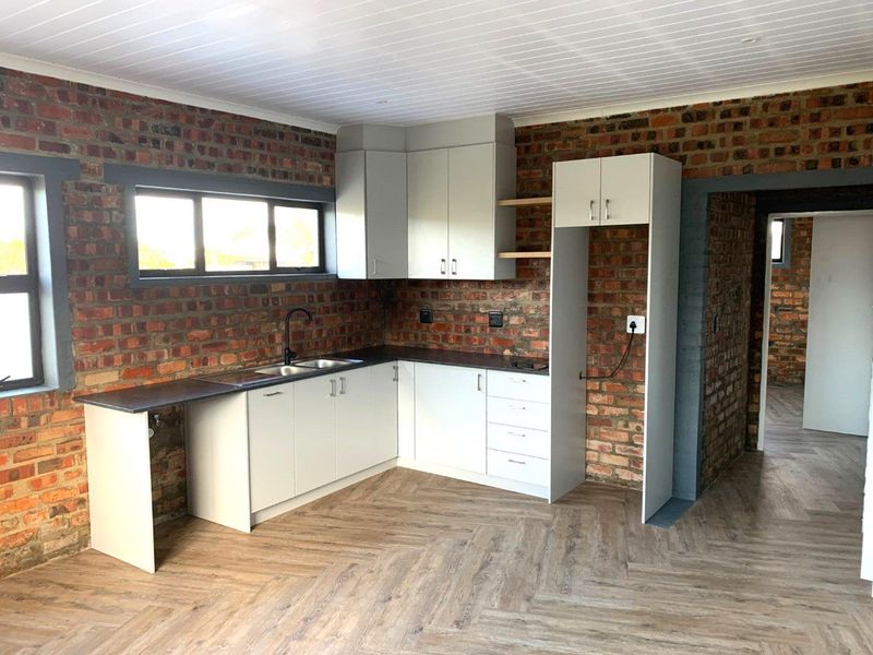 Modern kitchen featuring exposed brick walls, light grey cabinetry, double sink, and herringbone laminate flooring in an open-plan layout.