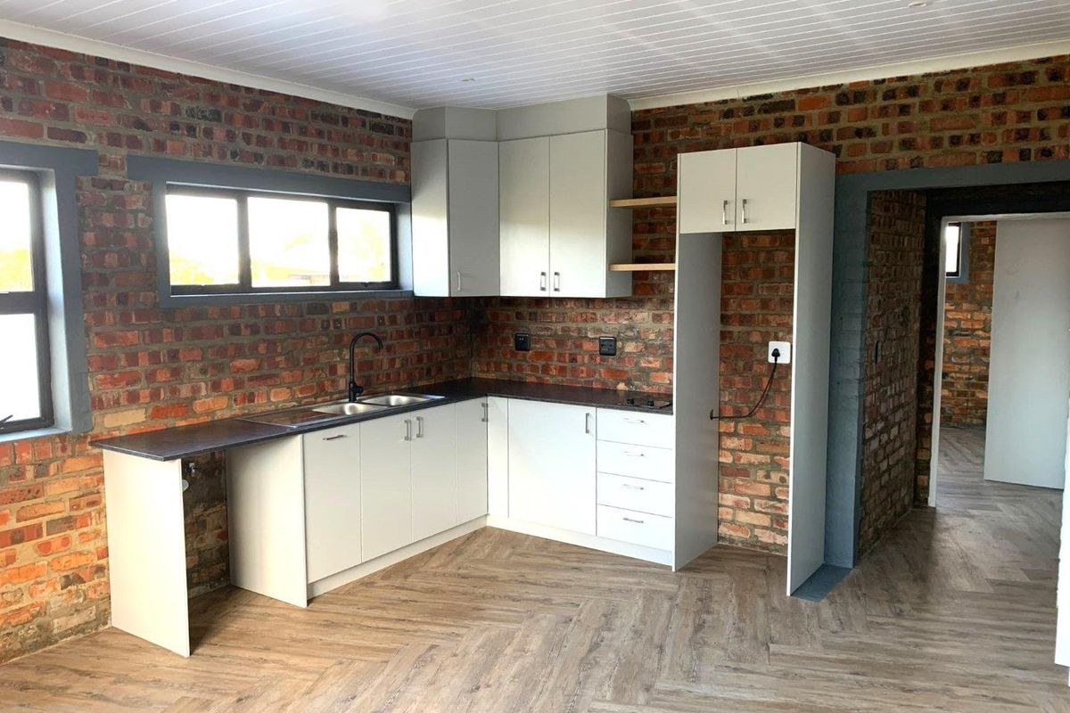 Modern kitchen featuring exposed brick walls, light grey cabinetry, double sink, and herringbone laminate flooring in an open-plan layout.