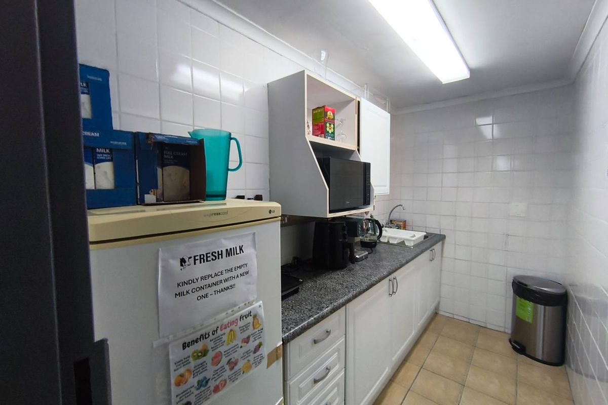 A functional kitchenette featuring white cabinetry, granite countertops, tiled walls, and tiled flooring, suitable for office or industrial staff use.