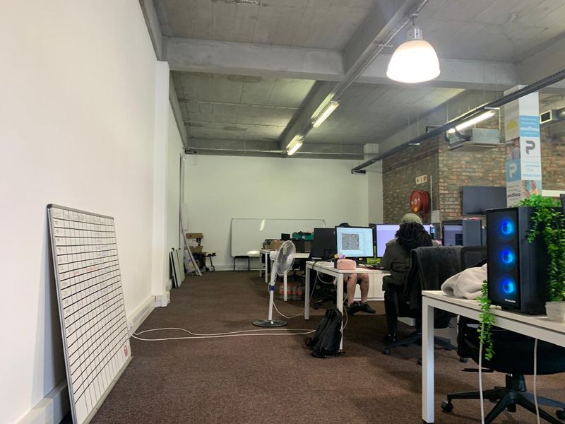 Open-plan office space featuring exposed concrete ceilings, brick accent wall, and carpeted flooring, providing a functional industrial-style work environment.