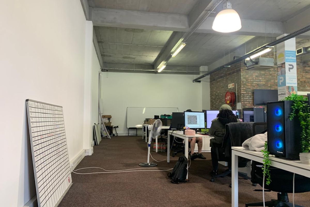 Open-plan office space featuring exposed concrete ceilings, brick accent wall, and carpeted flooring, providing a functional industrial-style work environment.
