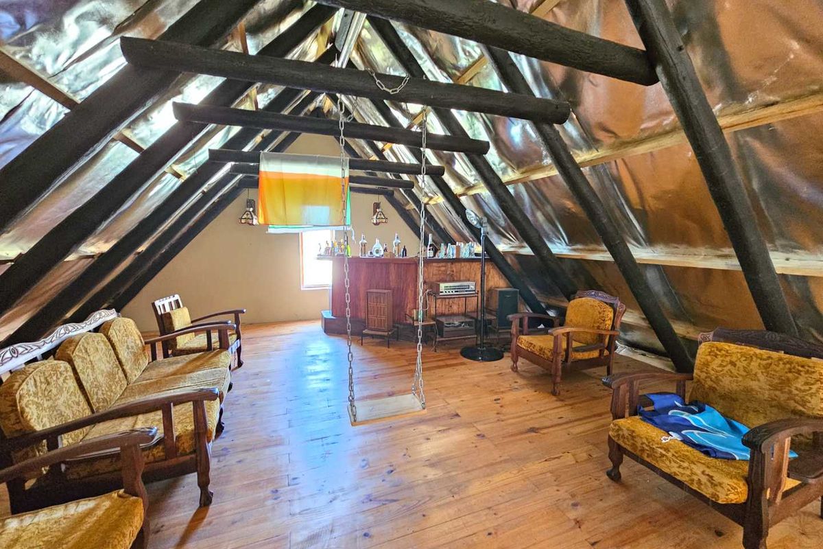 An attic-style living space featuring exposed timber roof trusses, reflective insulation lining, and a built-in bar area with timber flooring.