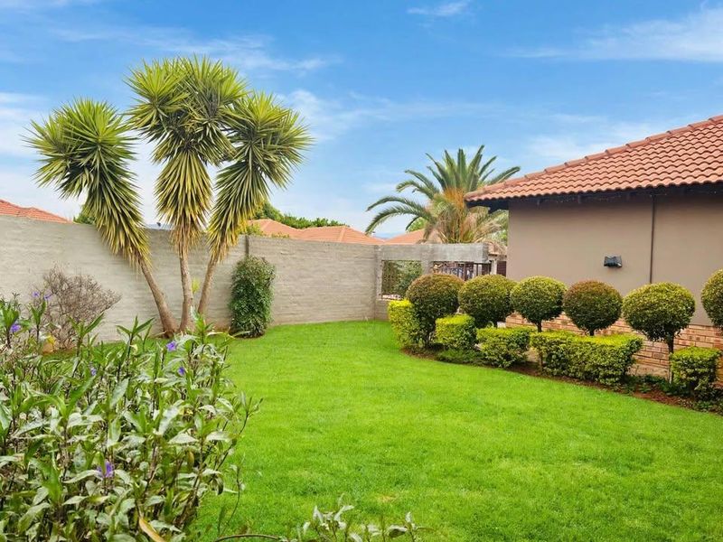 A well-maintained rear garden featuring a lush green lawn, manicured hedges, and a perimeter boundary wall, adjacent to the main house structure.