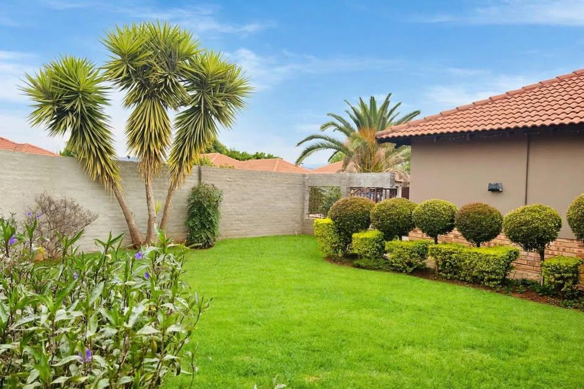 A well-maintained rear garden featuring a lush green lawn, manicured hedges, and a perimeter boundary wall, adjacent to the main house structure.